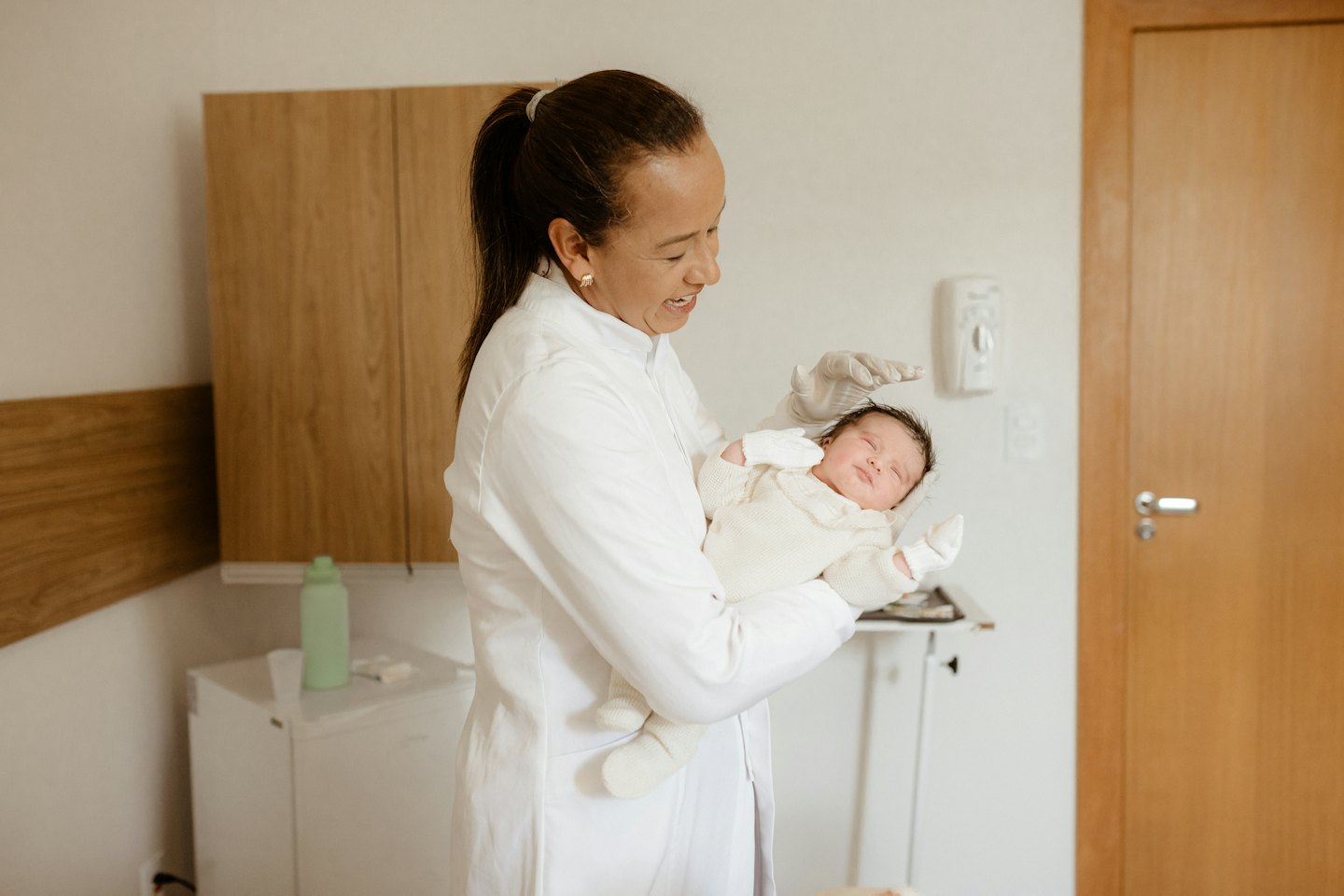 A doctor in a white lab coat holds a sleeping baby.